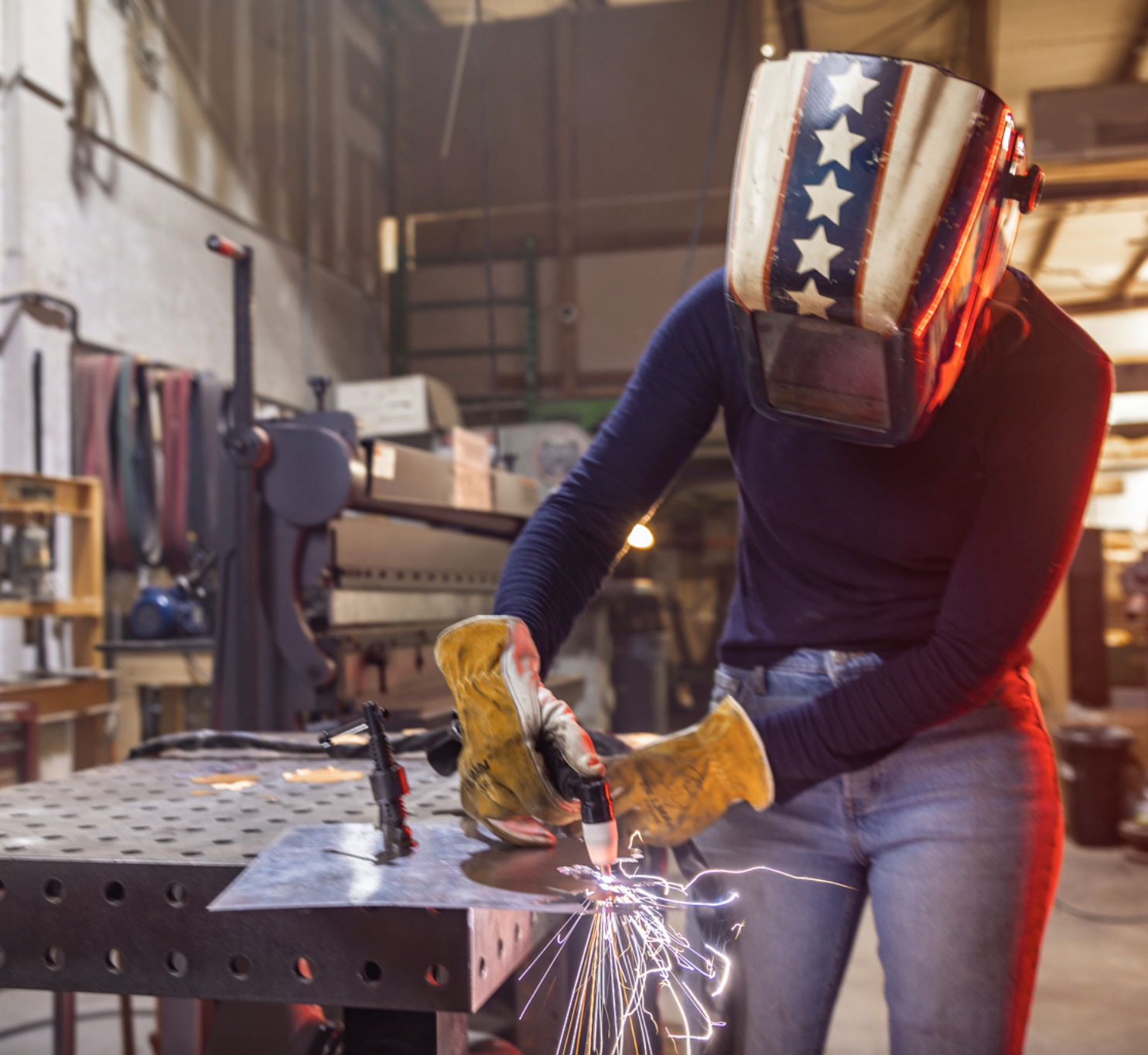 Asmbly Makerspace with a person welding wearing an American flag helmet in an industrial workshop