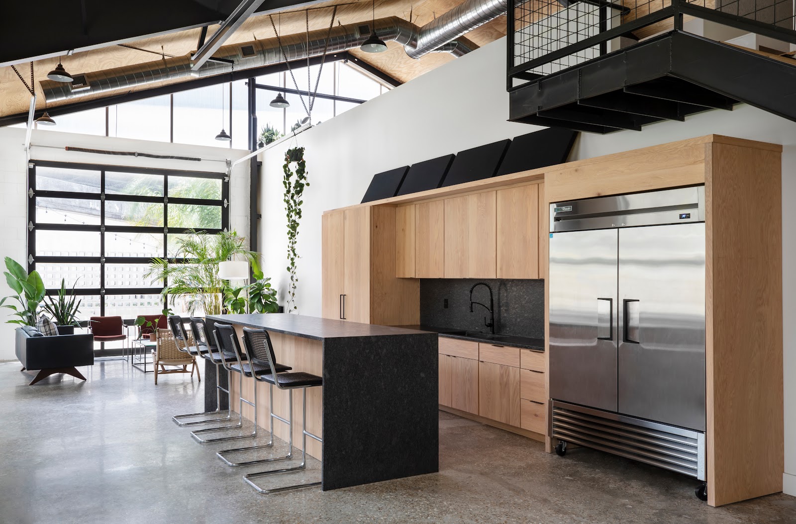 The Stables converted space with double-height ceilings, glass garage door, black stone kitchen island with bar stools, and natural oak cabinetry