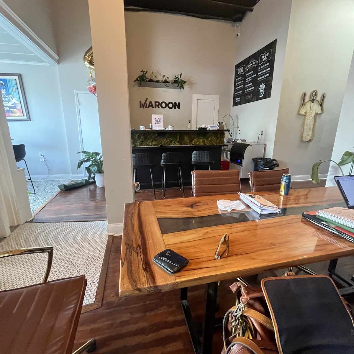 Maroon cafe-style coworking with live-edge wood table, brown leather chairs, moss-covered bar counter, MAROON wall signage, and eclectic decor
