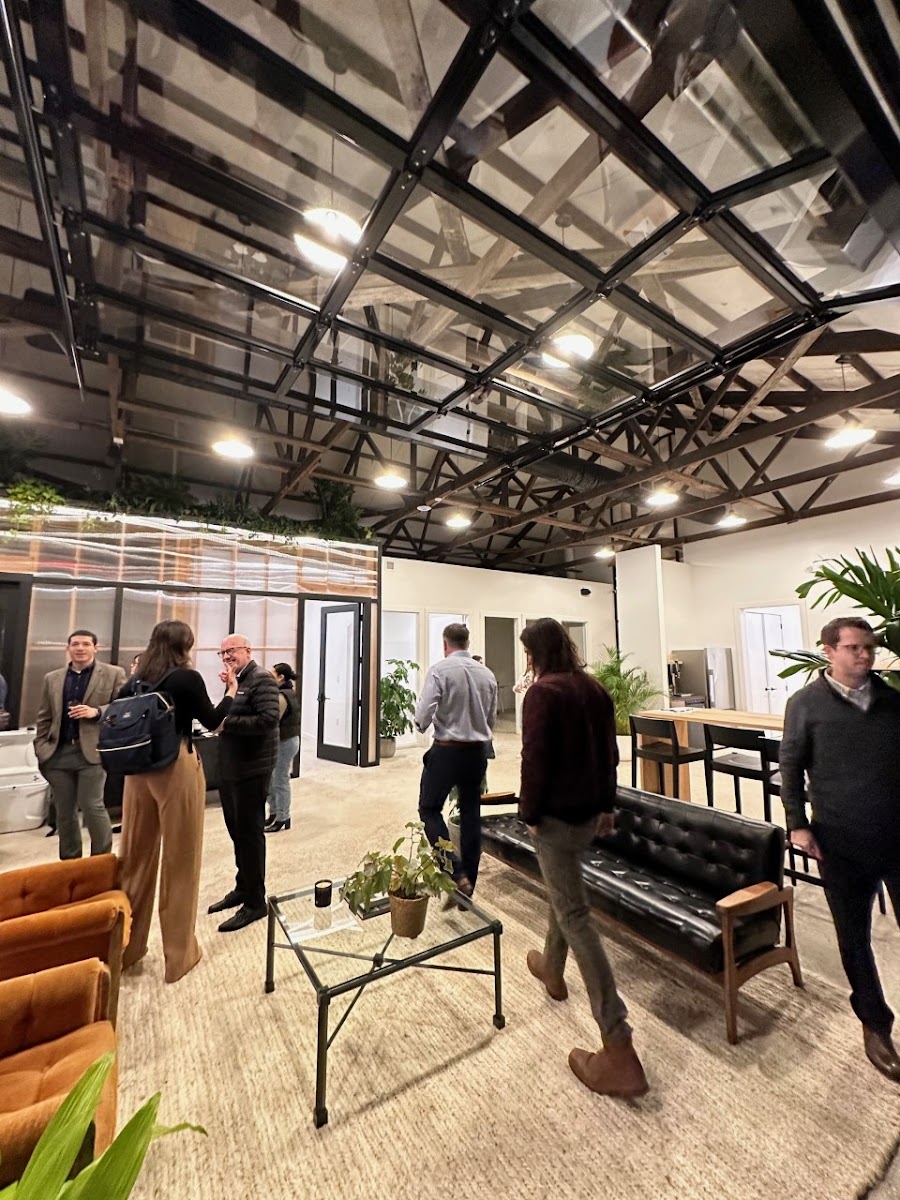 Greenhouse Workspace networking event with exposed steel trusses, glass skylights, orange leather chairs, black tufted bench, and potted plants